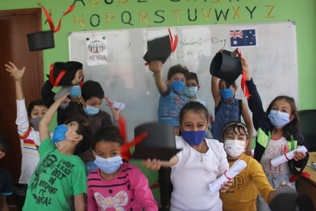 A jubilant grade one class celebrate by throwing their graduation hats in the air
